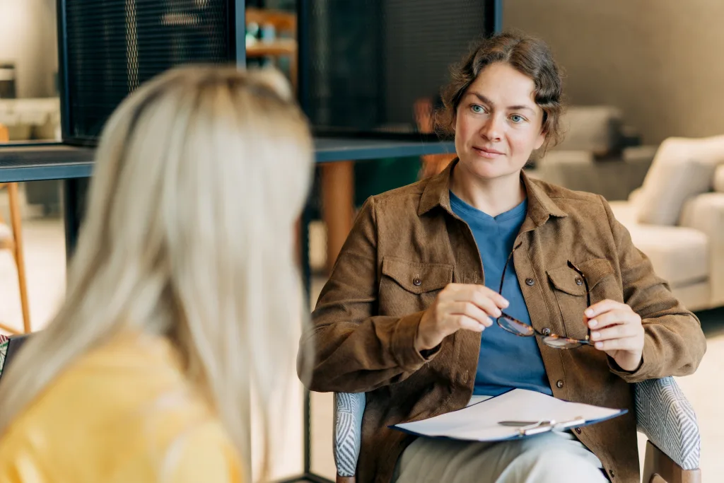 A tutor attentively listening to a student during an academic support session, holding notes and glasses
